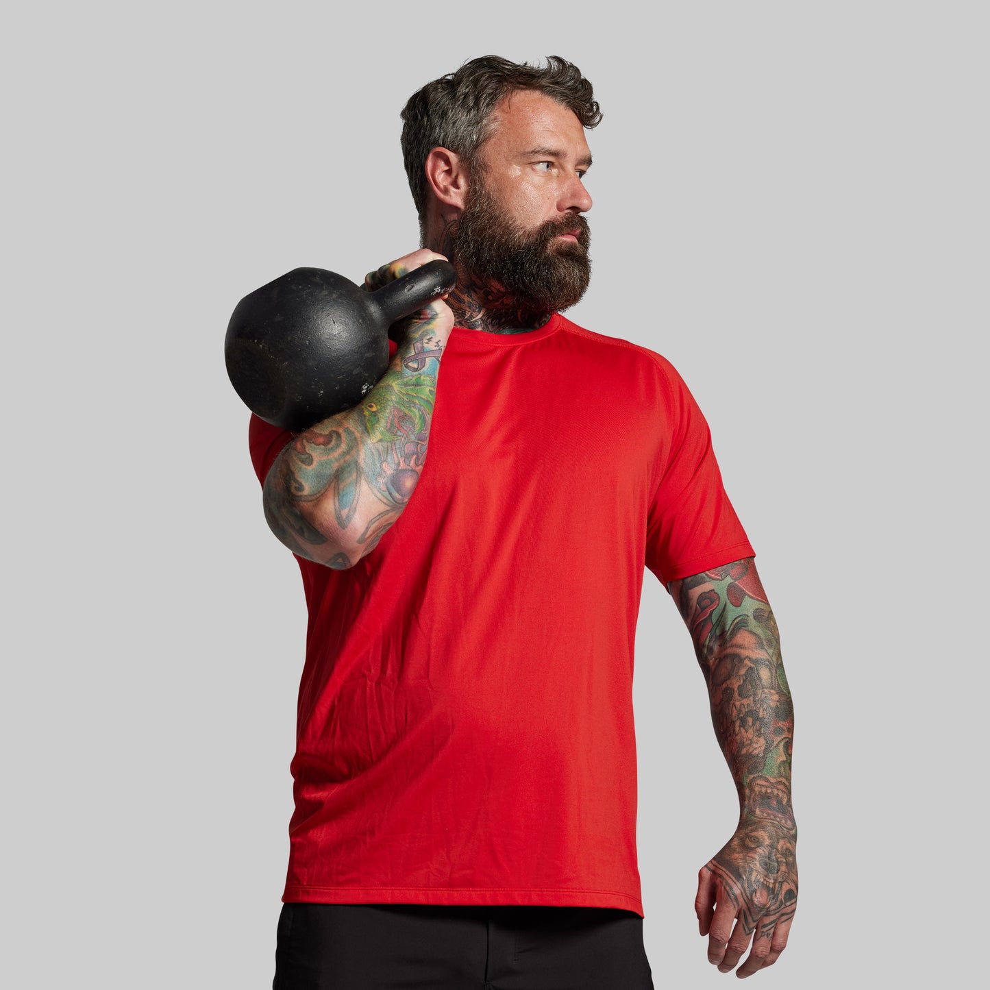 Man in a red shirt holding a black kettlebell against a gray background