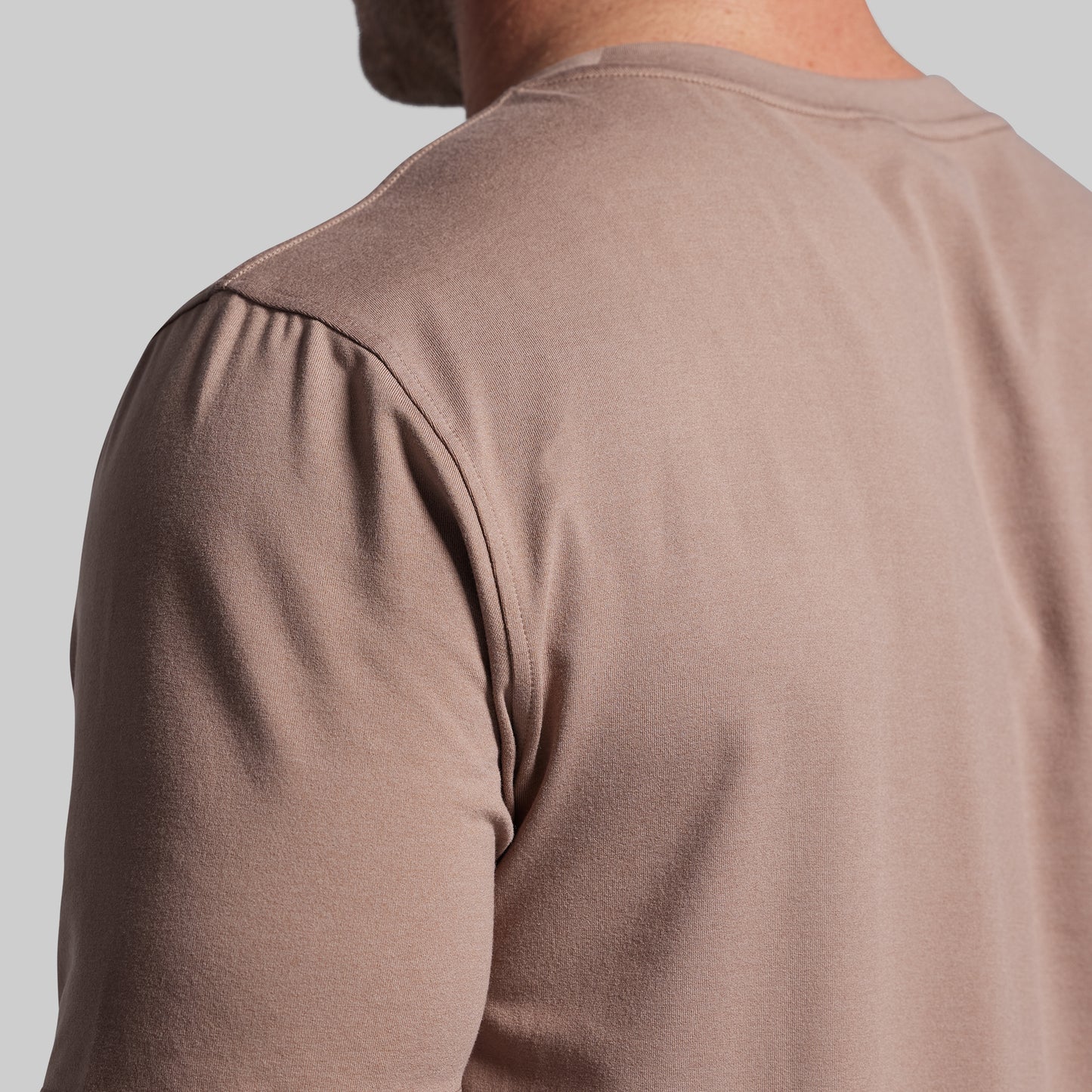 Close-up of a person wearing a brown shirt against a light gray background