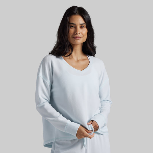 A woman modeling a light blue long-sleeve V-neck top against a solid light gray background.