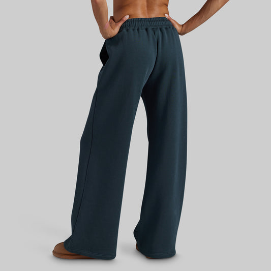 A person shown from the back wearing dark teal wide-leg sweatpants, standing against a solid light gray background.