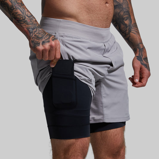 A person wearing light gray versatile shorts with a black compression liner and a phone held in the pocket.