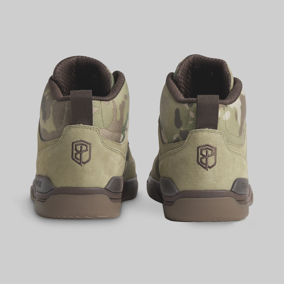 A pair of mid-top sneakers shown from the back, featuring a camouflage pattern in olive green, tan, and brown, with a dark brown heel pull tab and a geometric logo on the heel.