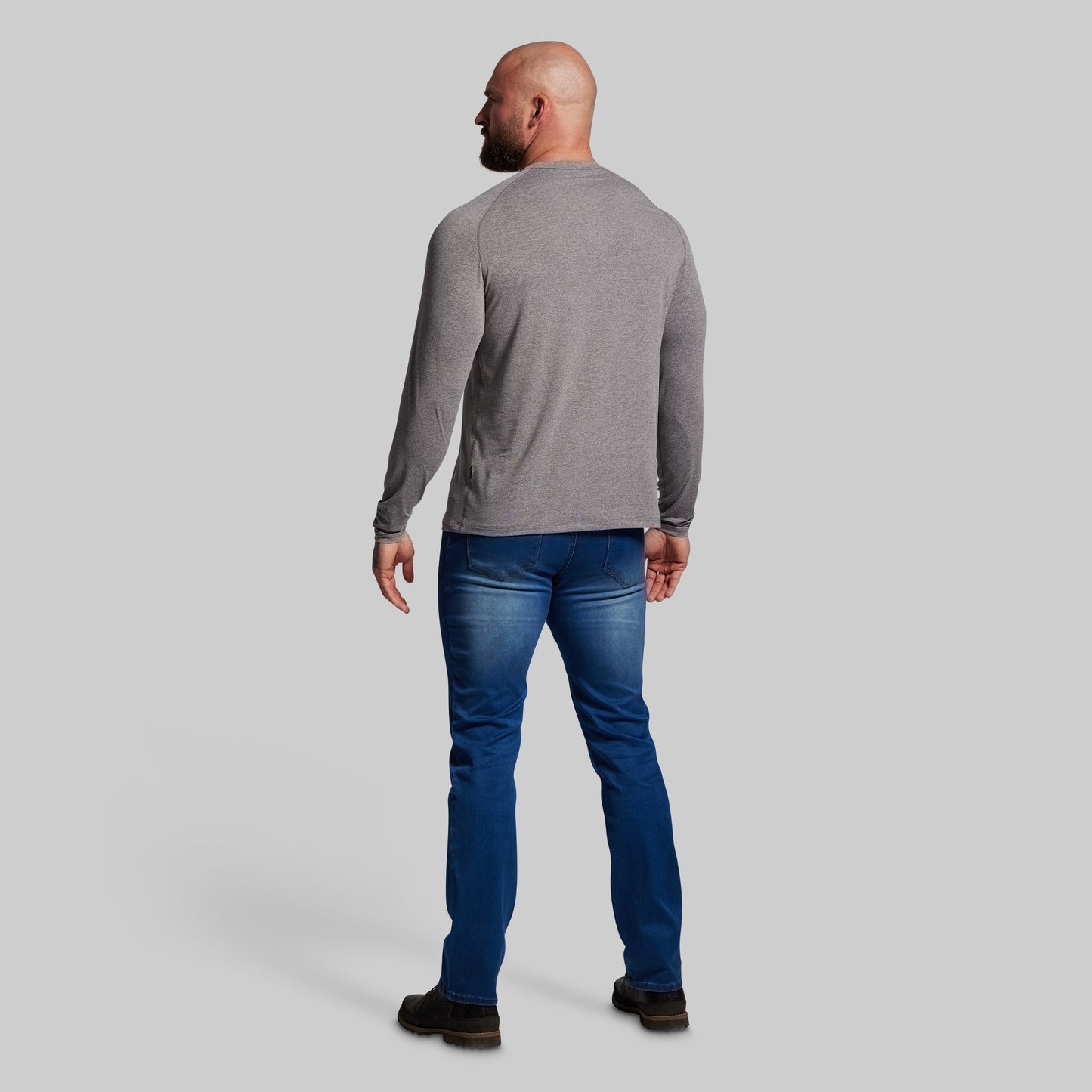 Man wearing a gray long-sleeve shirt and blue jeans on a light gray background