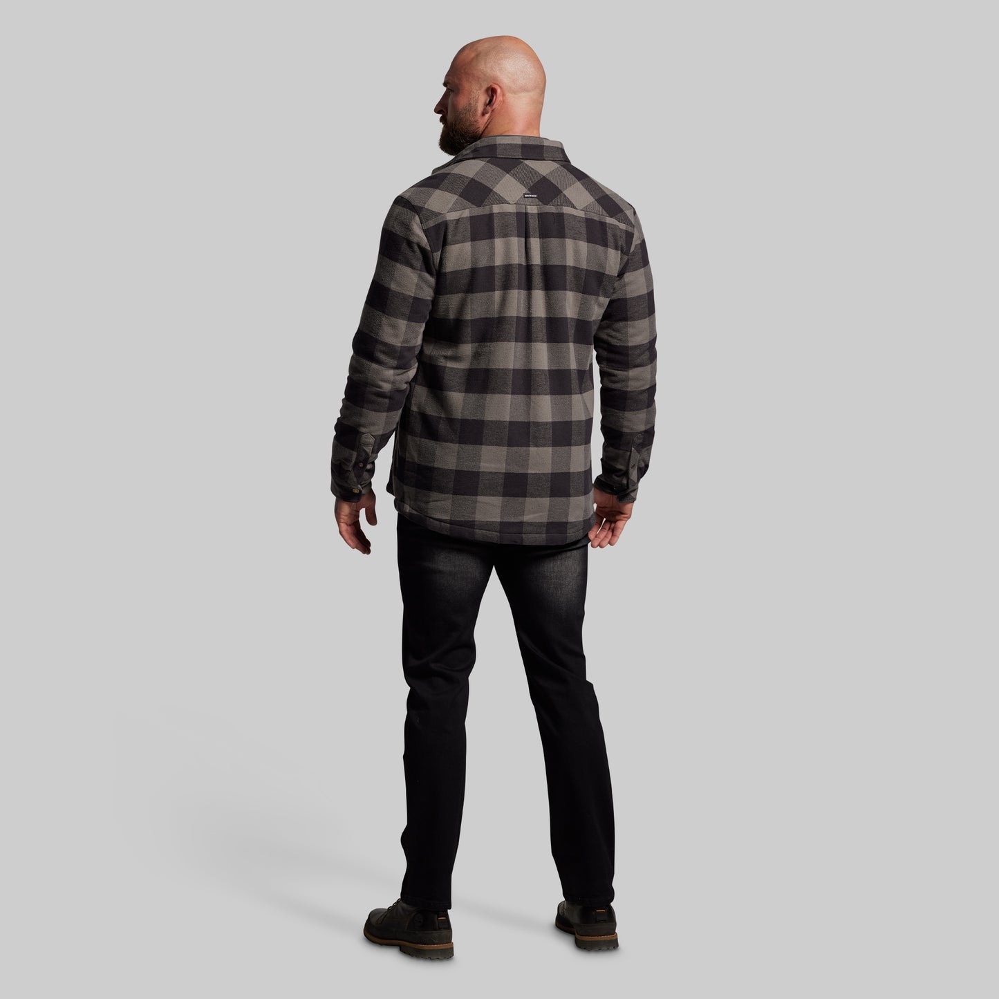 Man wearing a plaid jacket and black pants on a gray background