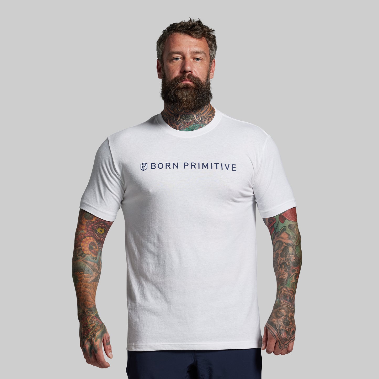 Man wearing a white 'Born Primitive' t-shirt against a gray background