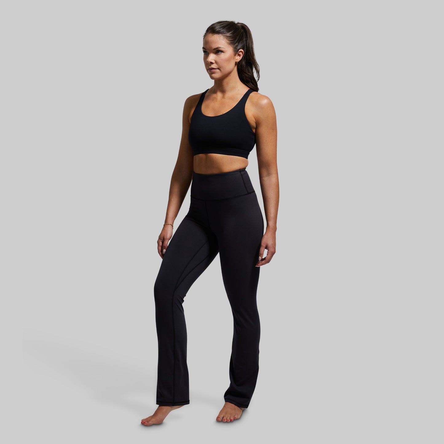 Woman wearing a black sports bra and yoga pants on a gray background