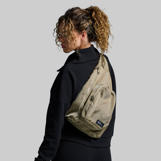 Person wearing a beige sling bag on a plain background