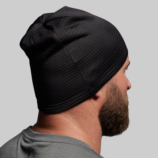 Person wearing a black beanie against a gray background
