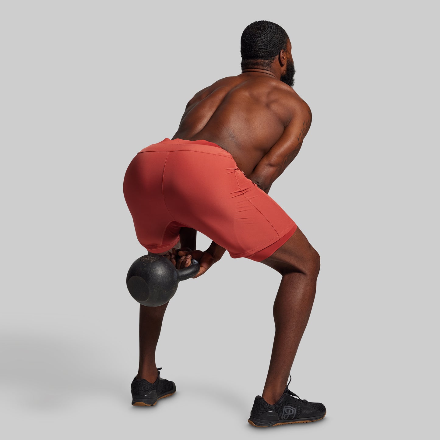 Man in red shorts performing a kettlebell exercise on a gray background