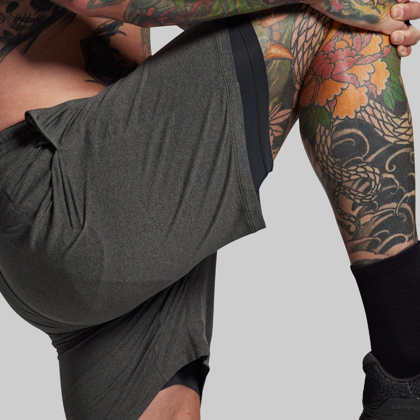 Person wearing dark gray athletic shorts with a tattooed arm on a light gray background