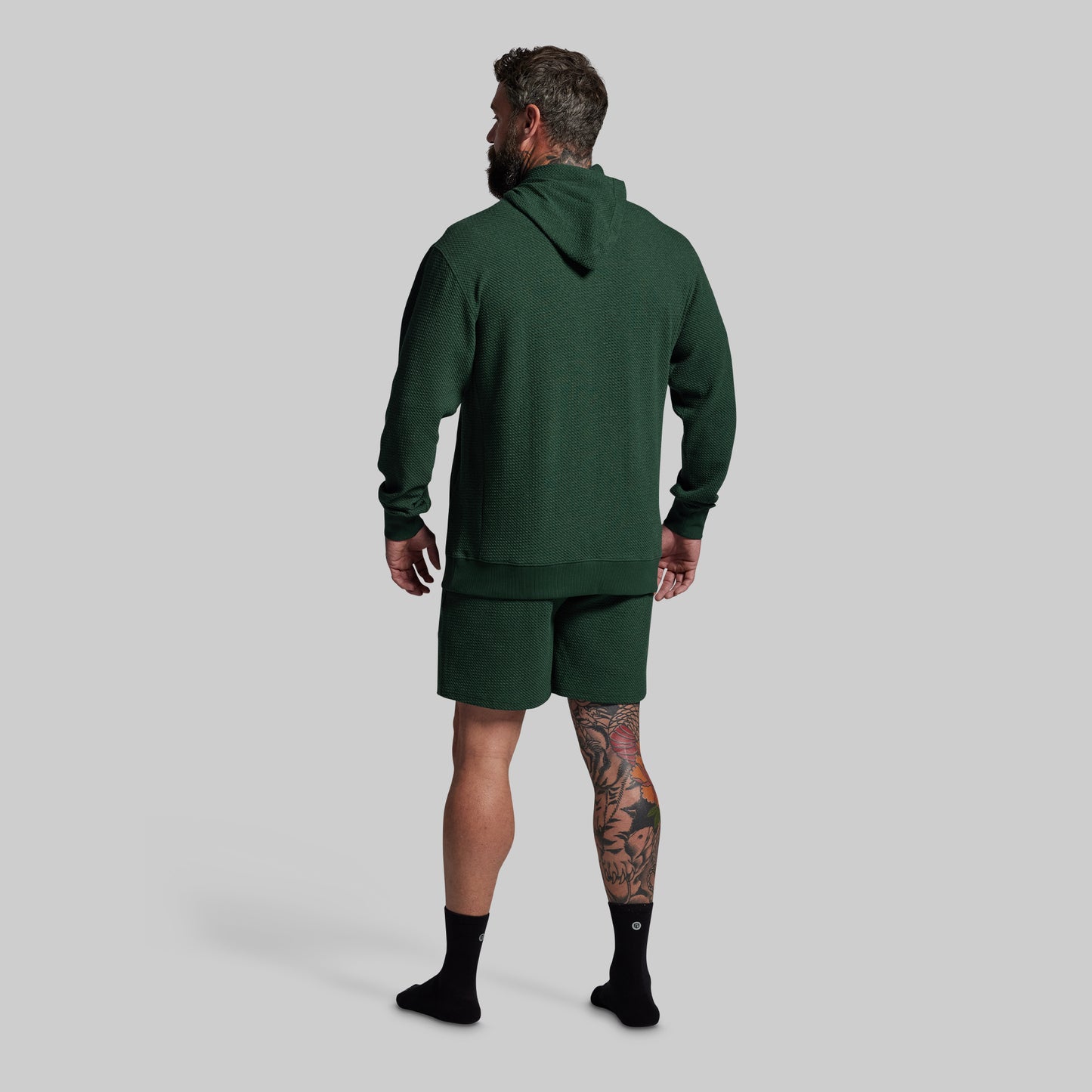 Man wearing a green hoodie and shorts set on a gray background