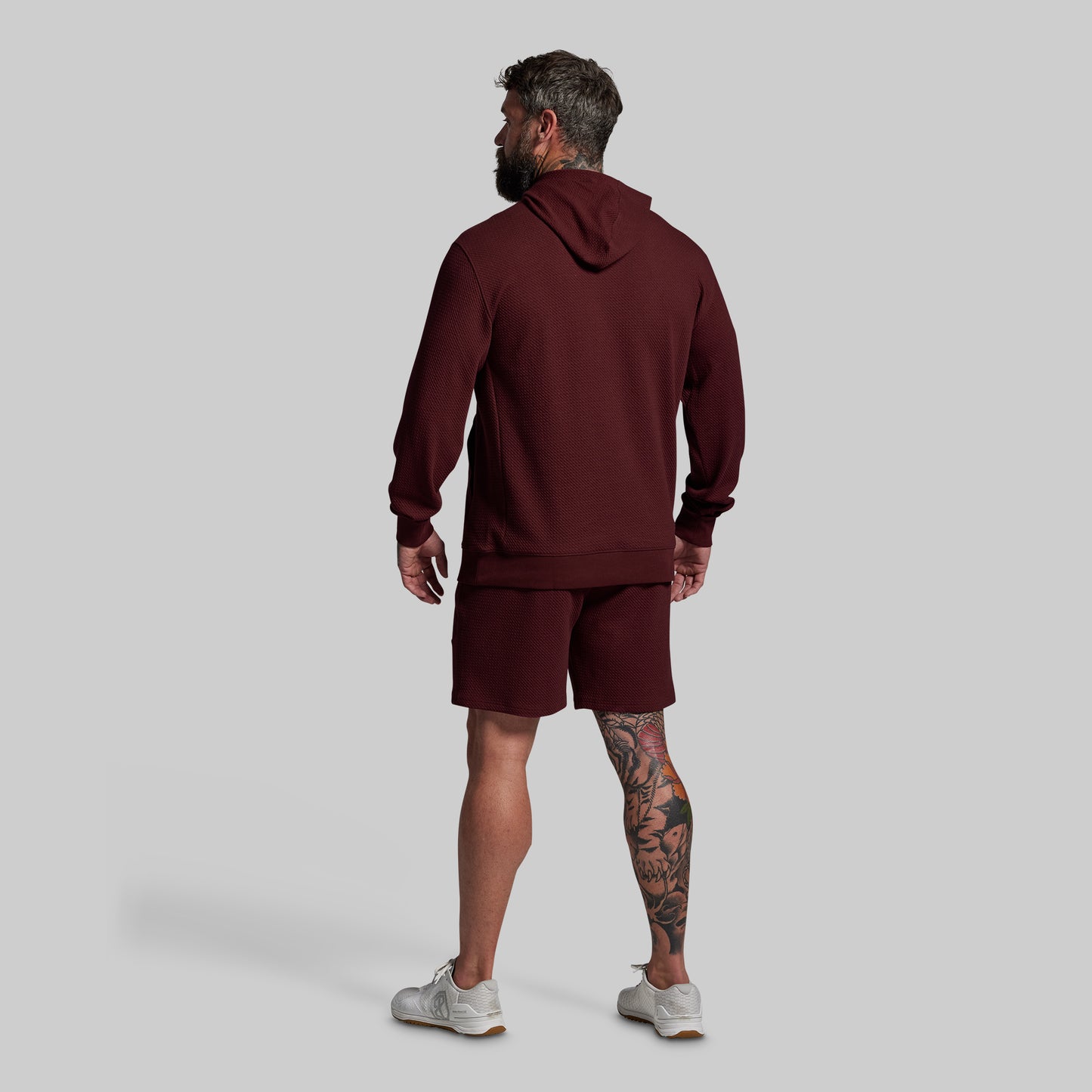 Man wearing a maroon hoodie and shorts set on a light gray background