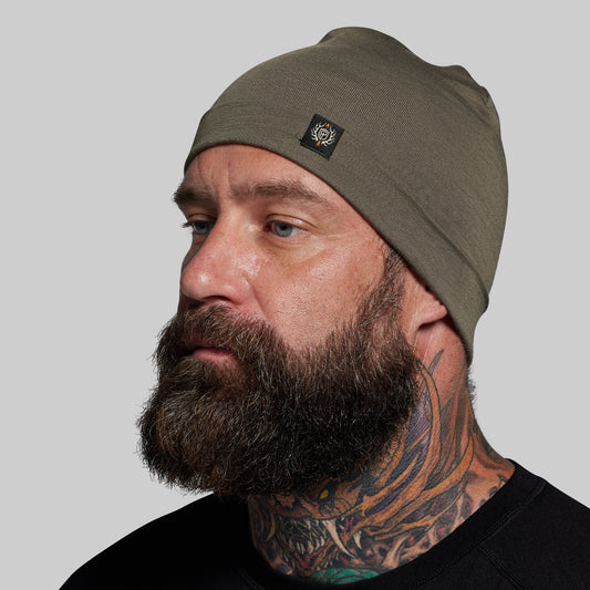 Man wearing a green beanie with a logo on a gray background