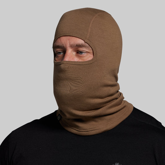 Person wearing a brown balaclava against a gray background
