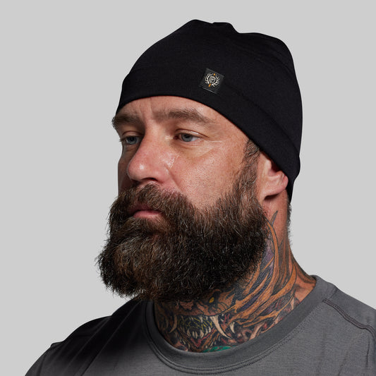 Man wearing a black beanie with a logo on a gray background