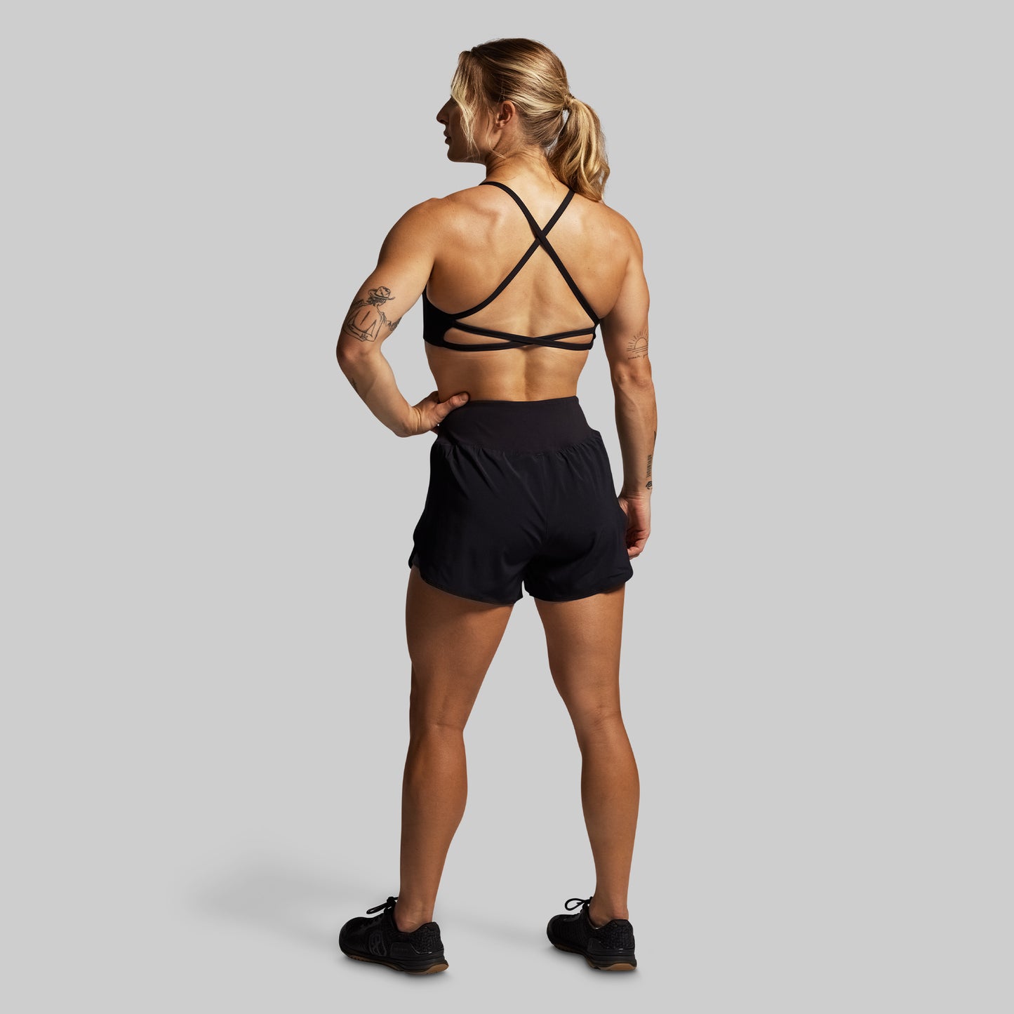 Woman wearing a black sports bra and shorts on a gray background