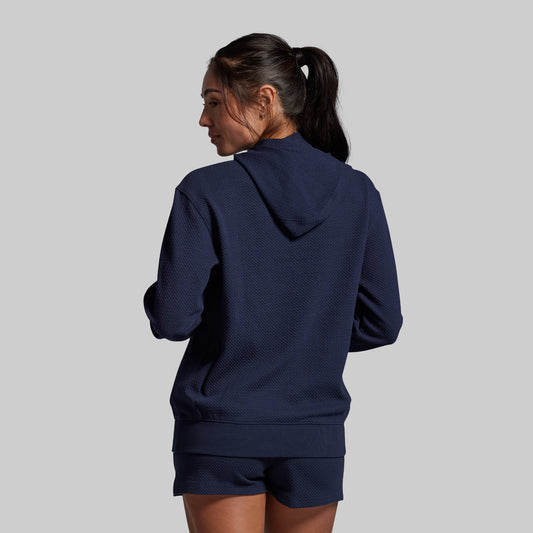 Person wearing a navy blue hoodie and shorts set on a gray background