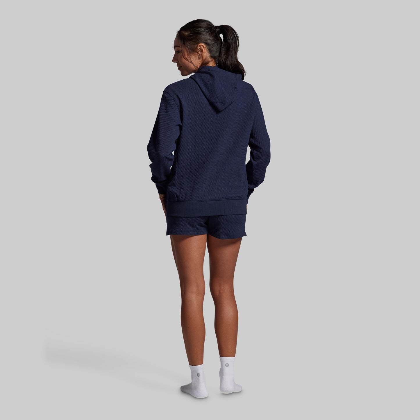 Person wearing a navy blue hoodie and shorts set on a light gray background