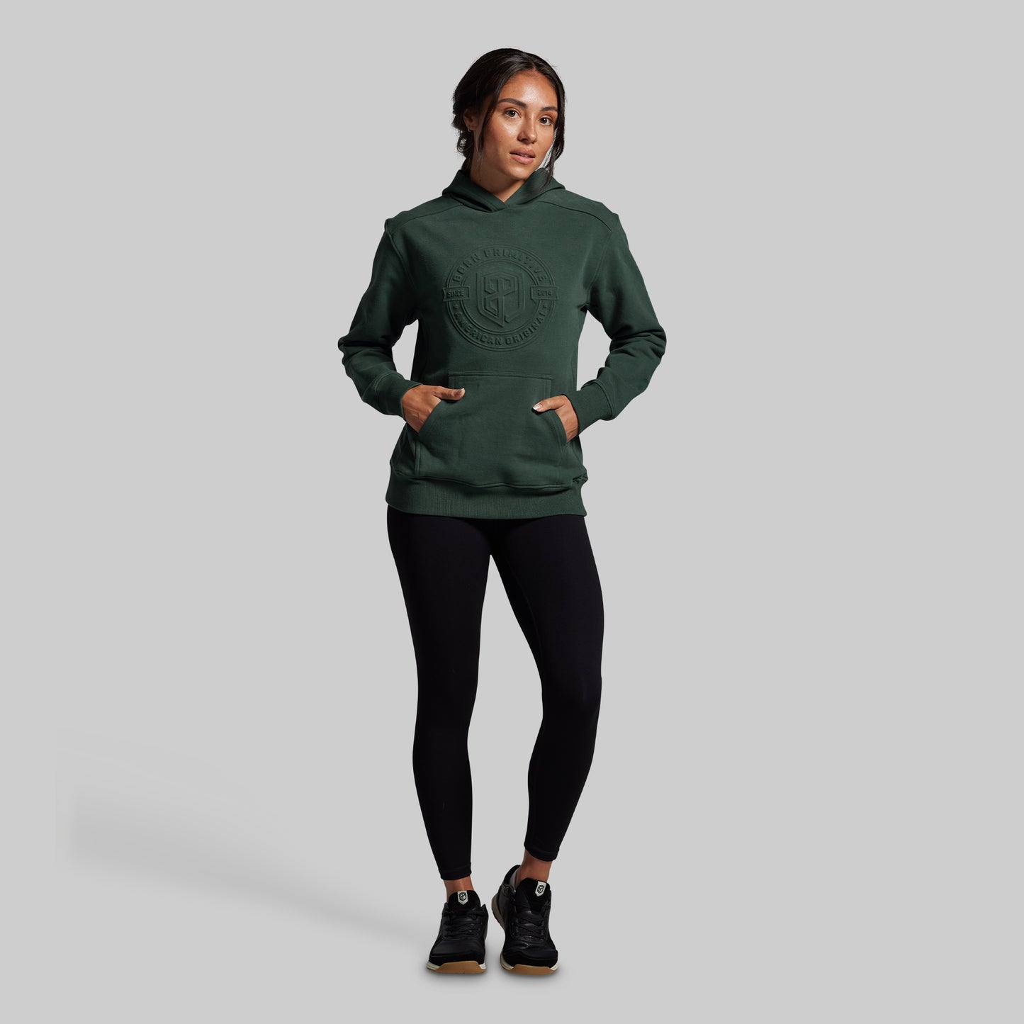 Person wearing a green hoodie and black leggings on a gray background