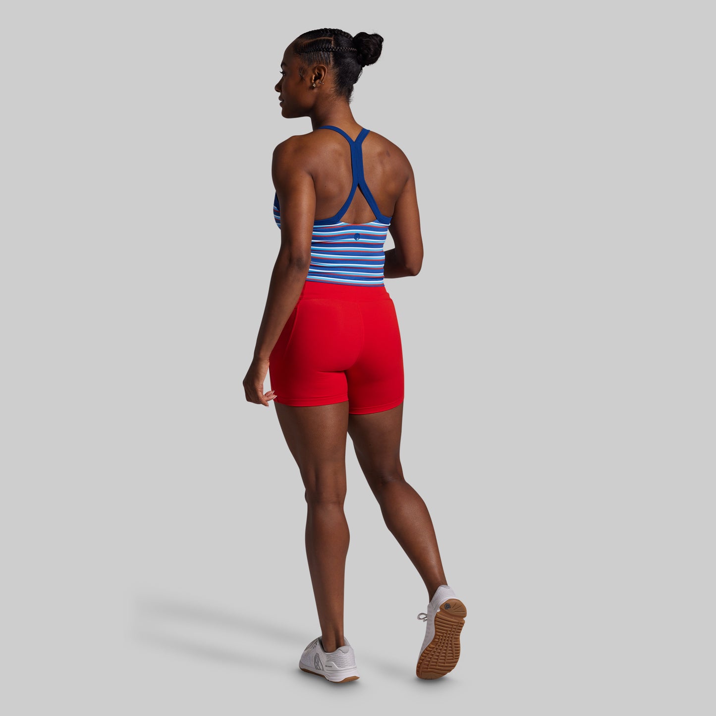 Woman wearing a blue and white striped sports bra and red shorts on a gray background
