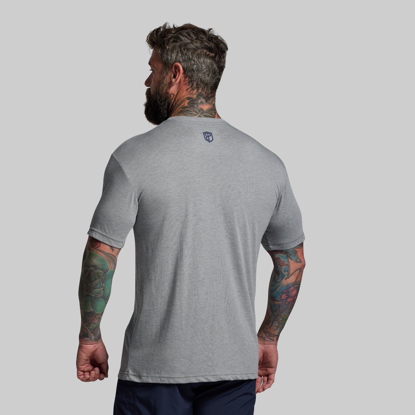 Man wearing a gray t-shirt with a logo on the back against a plain background