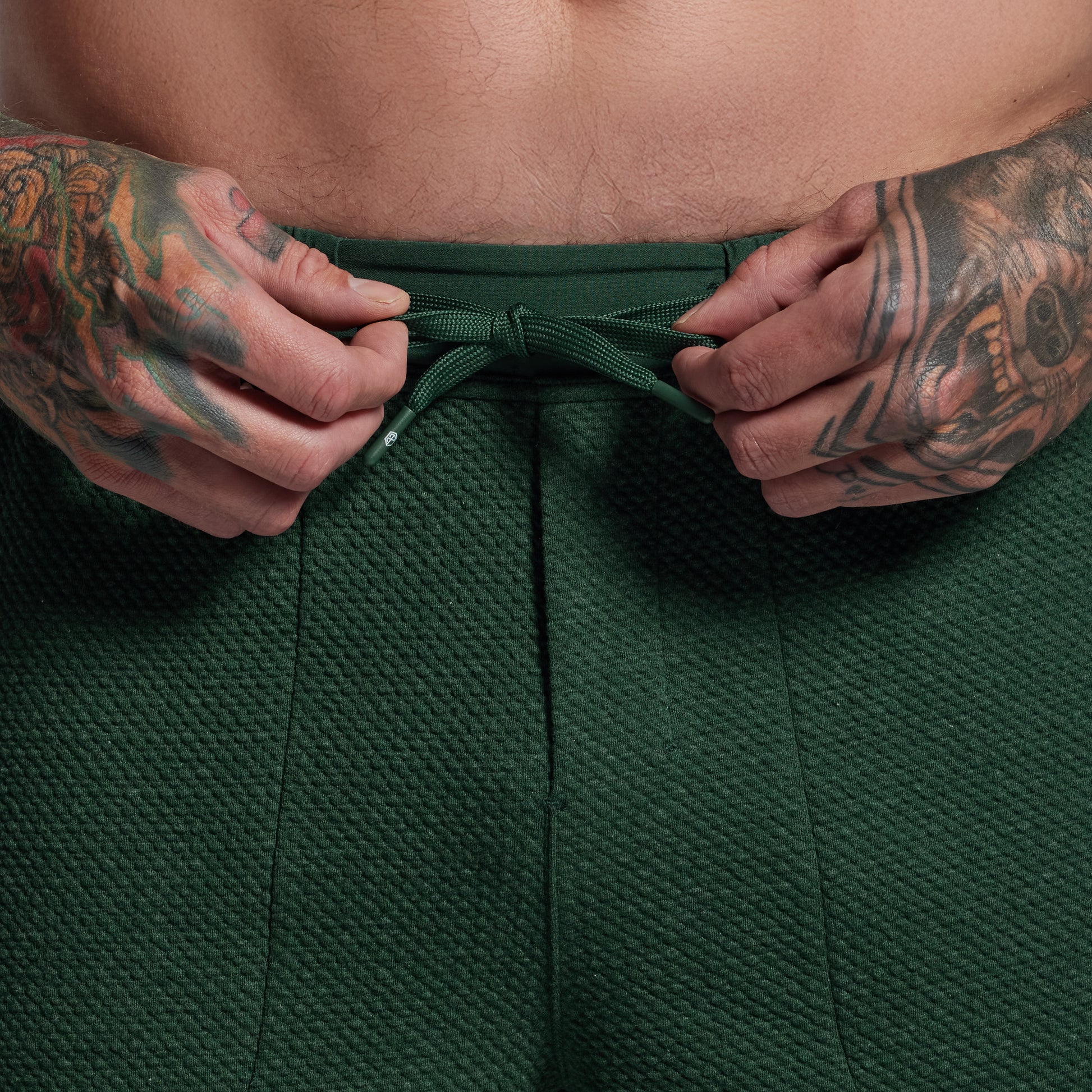 Person wearing green shorts with tattooed arms adjusting the waistband.