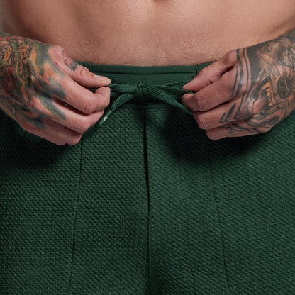 Person wearing green shorts with tattooed arms adjusting the waistband.