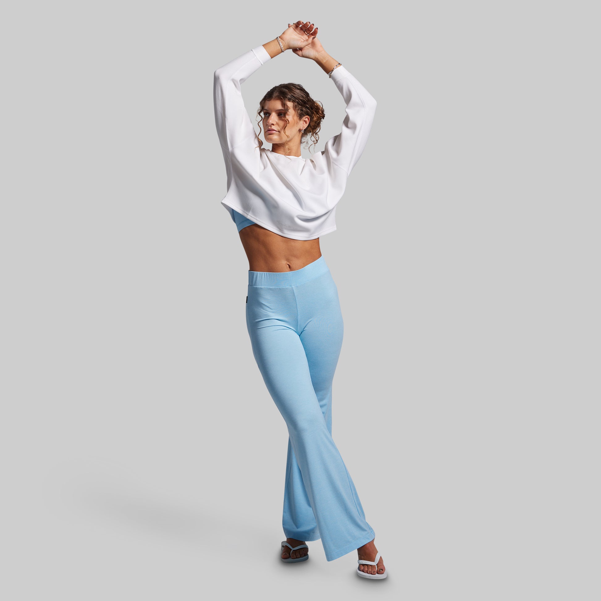 Woman wearing a white sweatshirt and light blue flared pants on a gray background