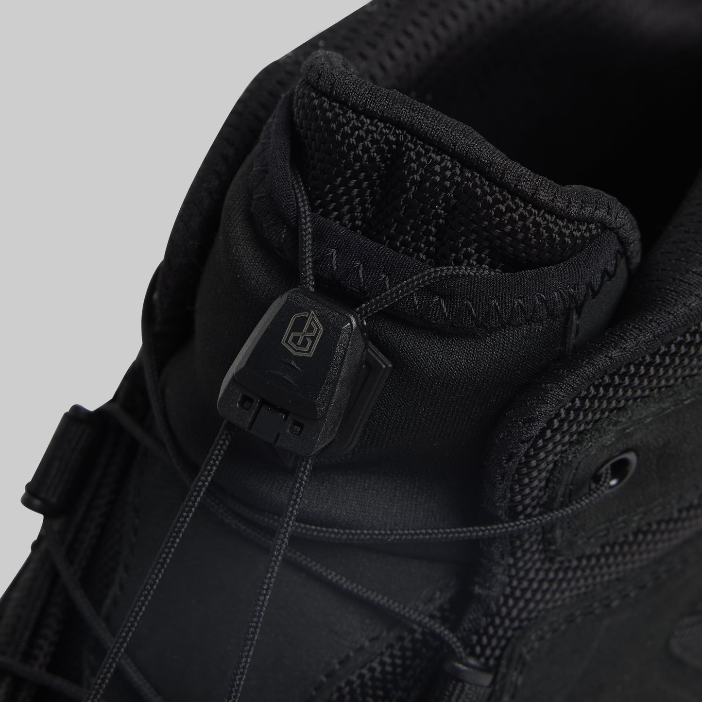 Close-up of a black tactical boot with a brand logo on a gray background