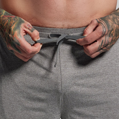 Person wearing gray shorts with tattooed hands adjusting the waistband.