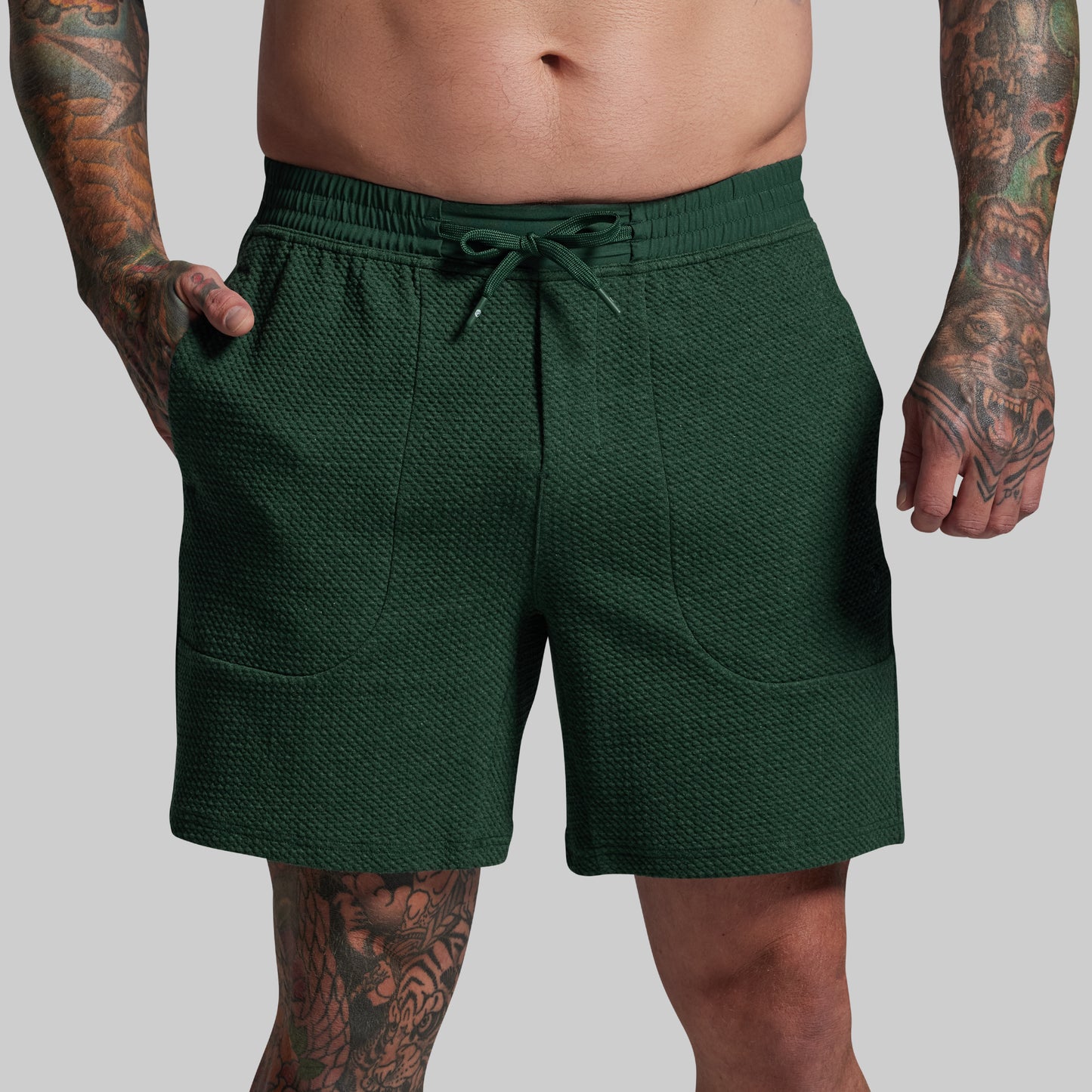 Green shorts worn by a person with tattoos on a gray background