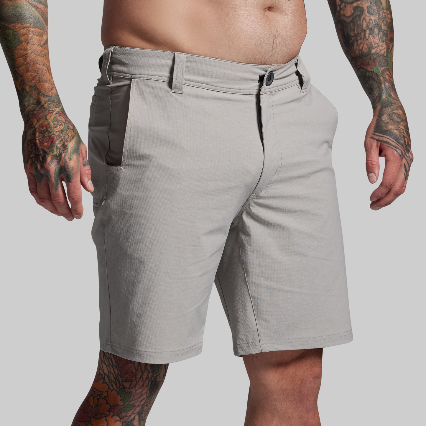 Gray shorts worn by a person with tattoos on a plain background