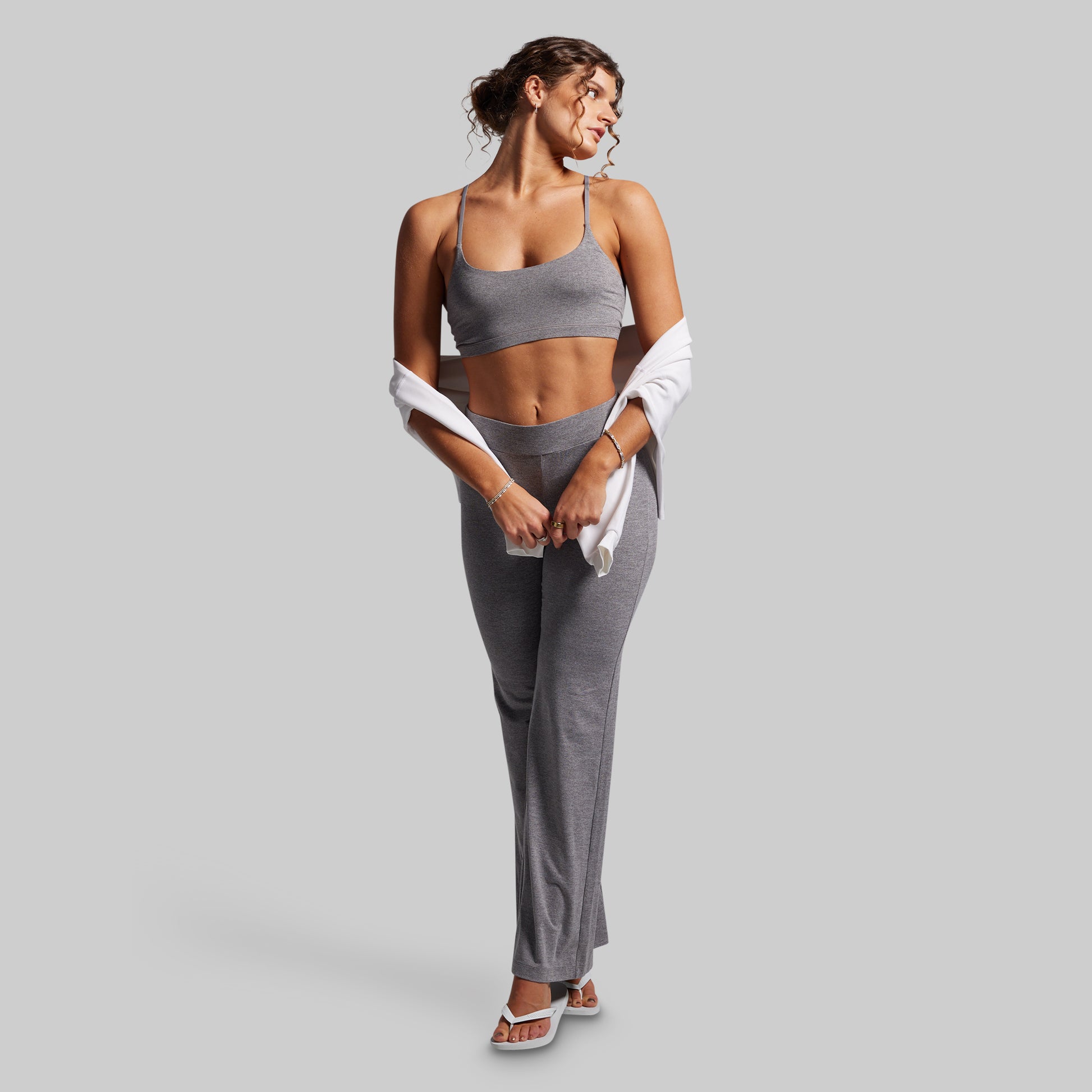 Woman in gray athletic wear holding a white sweatshirt on a light gray background
