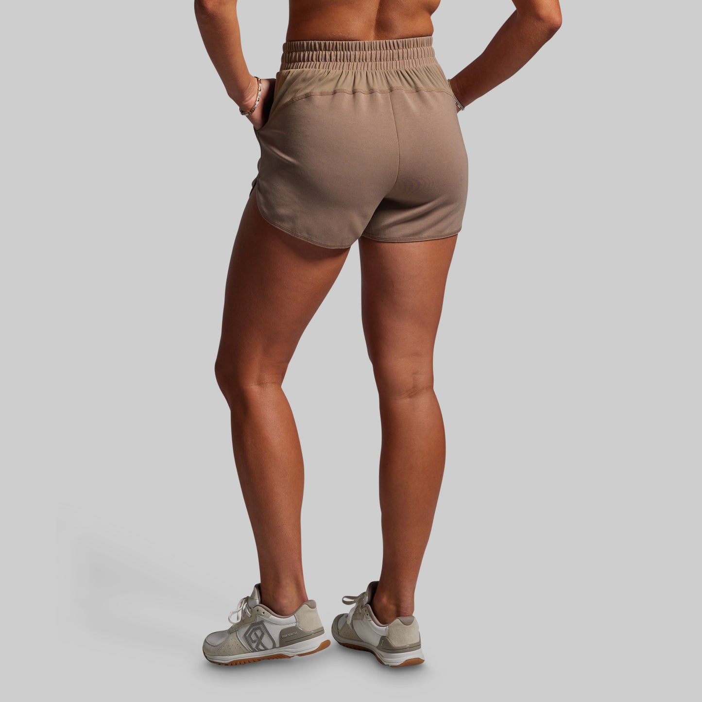 Person wearing beige athletic shorts on a plain background