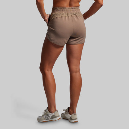 Person wearing beige athletic shorts on a plain background