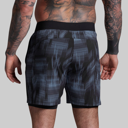 Person wearing black and gray patterned shorts on a plain background