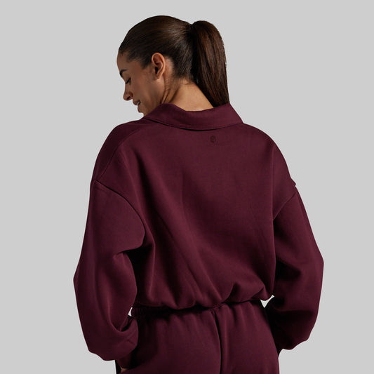 A woman shown from the back wearing a deep burgundy crewneck sweatshirt and matching drawstring sweatpants against a solid gray studio background.