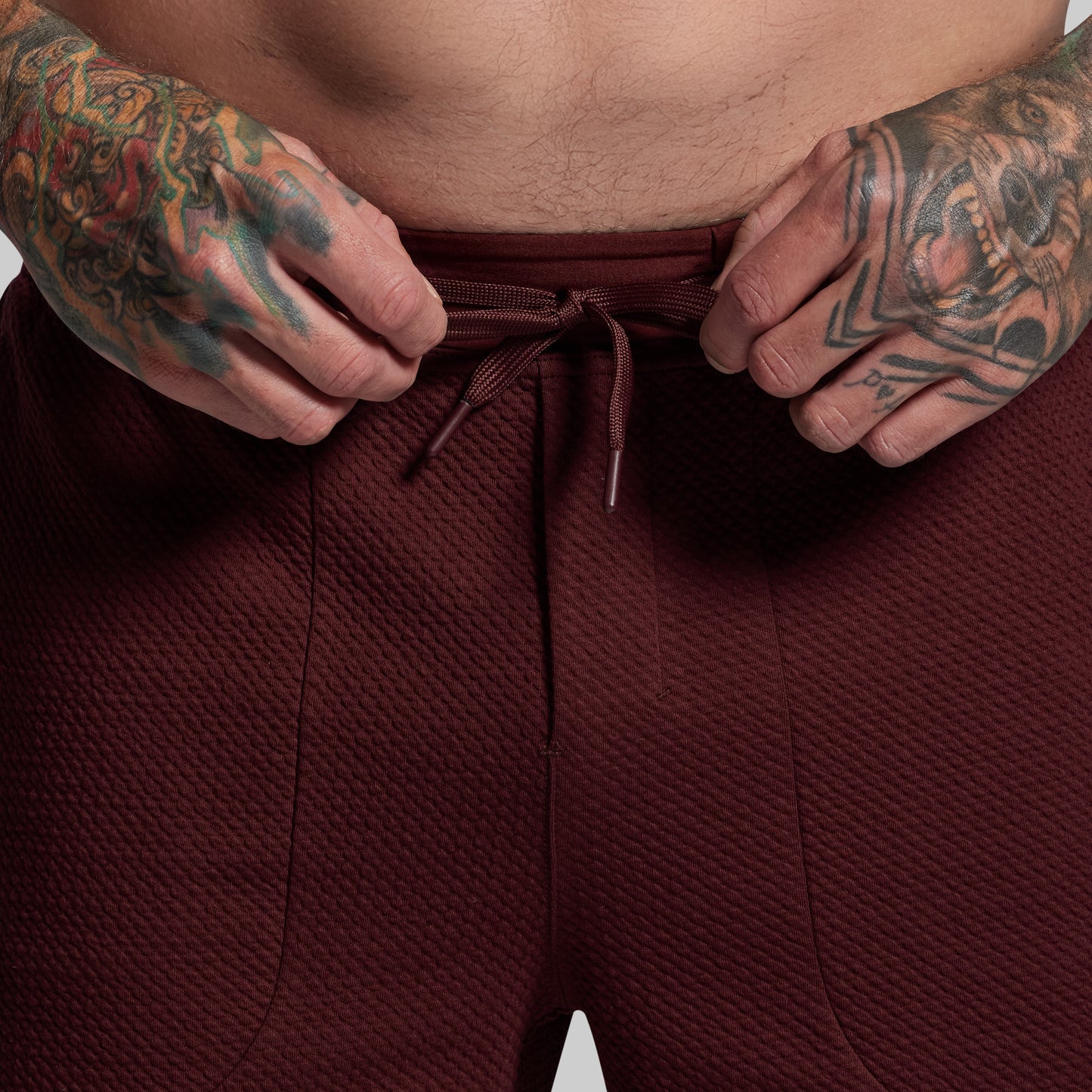 Person wearing maroon pants with tattooed hands adjusting the drawstring.
