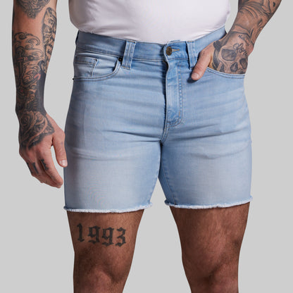 Person wearing light blue denim shorts with tattoos on arms and legs against a plain background