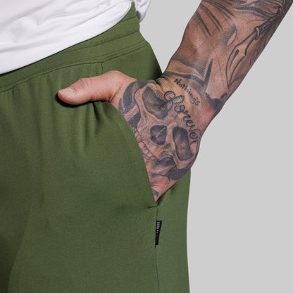 Person wearing green shorts with a tattooed arm on a plain background