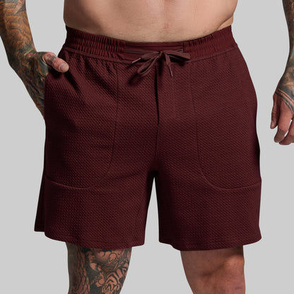 Maroon shorts worn by a person with tattoos on a gray background