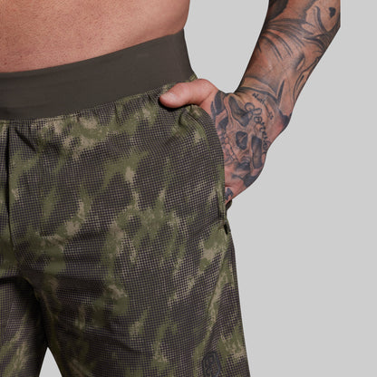 Person wearing camouflage shorts with a tattooed arm on a gray background