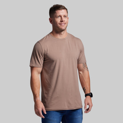 Man wearing a brown t-shirt and blue jeans against a gray background