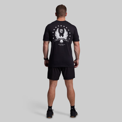 Man wearing a black t-shirt with a white graphic on the back and black shorts against a gray background