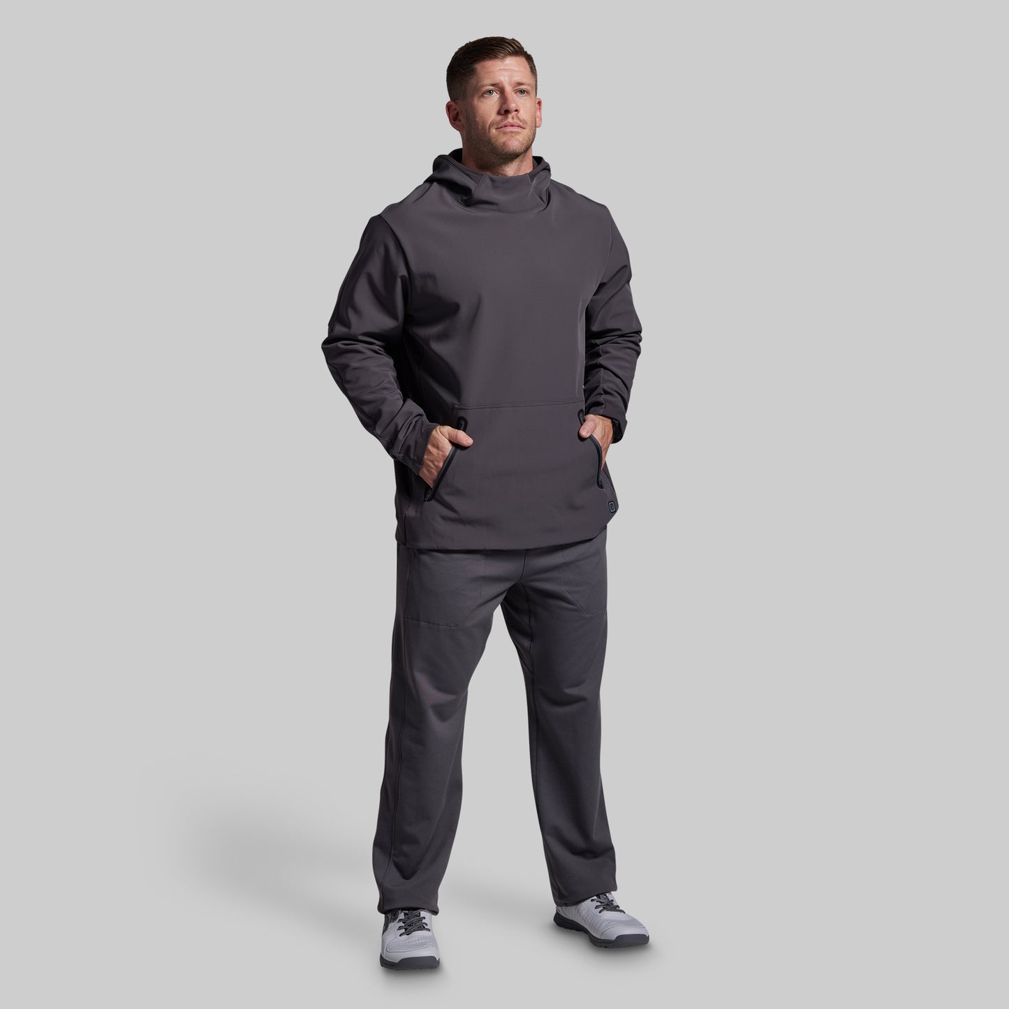 Man wearing a dark gray hoodie and pants on a light gray background