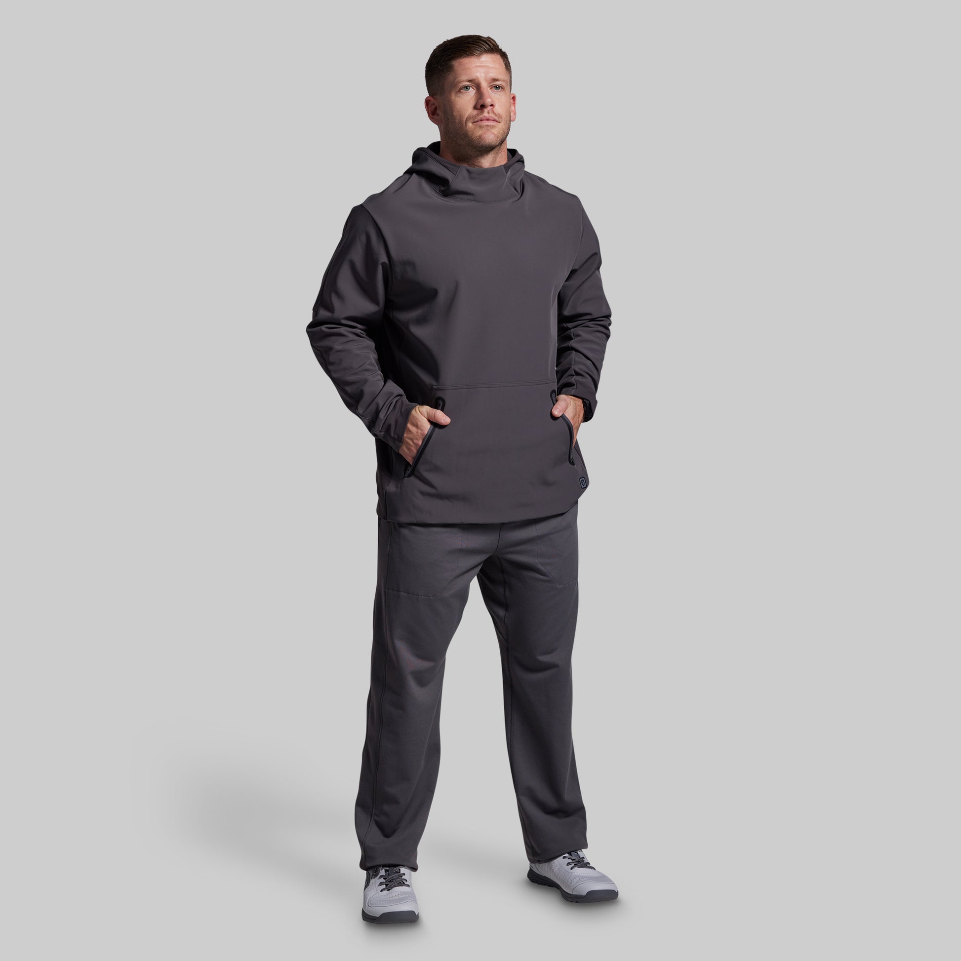 Man wearing a dark gray hoodie and pants on a light gray background