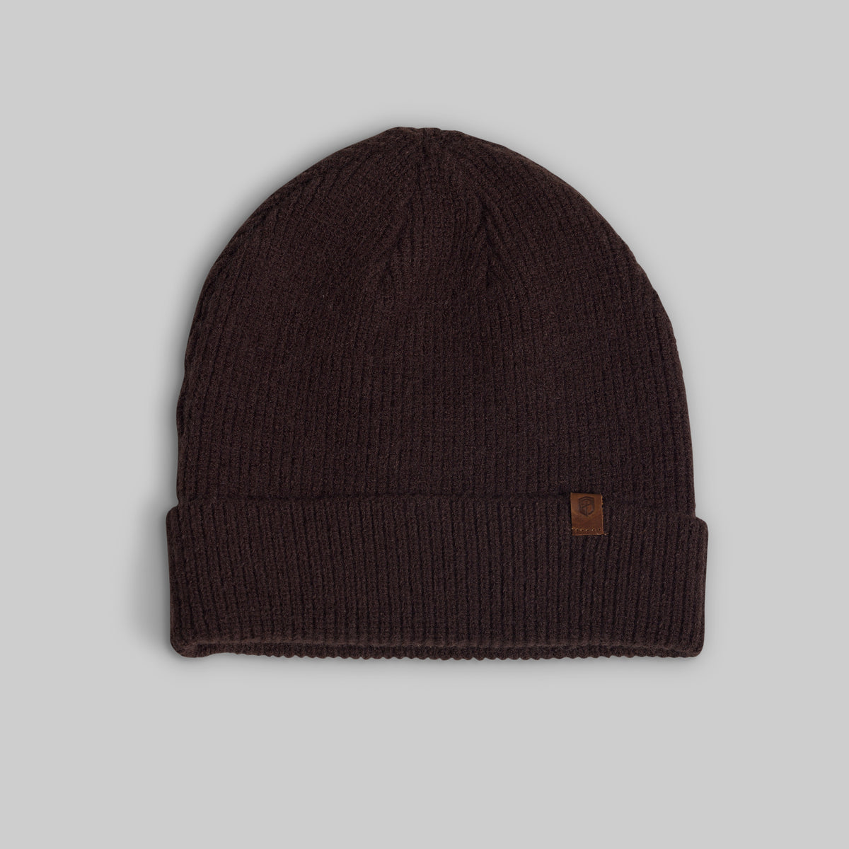 A dark brown ribbed knit beanie hat with a small brown leather logo patch on the side, displayed against a neutral gray background.