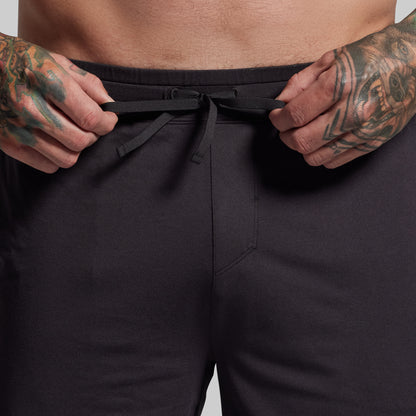 Person wearing black shorts with tattooed hands adjusting the waistband against a neutral background