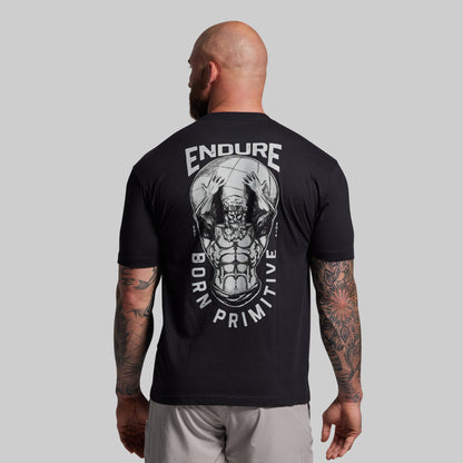 Man wearing a black t-shirt with 'Endure Born Primitive' design on the back against a gray background