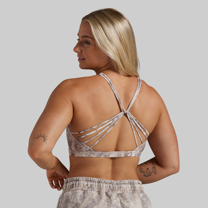 A woman shown from the back wearing a strappy sports bra and matching patterned sweatpants against a plain light gray studio background.